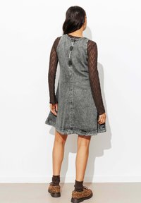 Robe en denim gris avec une forme évasée, fermeture éclair au dos et manches longues en dentelle noire. Associée à des bottes à imprimé léopard marron et des chaussettes en tricot.