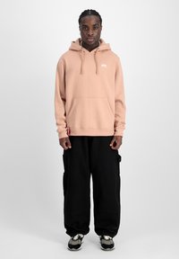Felpa con cappuccio beige, dotata di tasca frontale e cordini, abbinata a pantaloni cargo neri di taglio loose e sneakers nere.