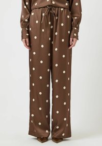 Brune vide bukser i et silkeaktig stoff, med store kremfargede polkadotter og snor i midjen, med lange ermer og knappedetaljer.