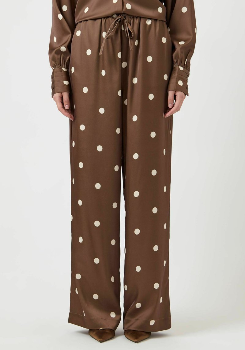 Brune vide bukser i et silkeaktig stoff, med store kremfargede polkadotter og snor i midjen, med lange ermer og knappedetaljer.