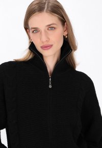 Maglione nero lavorato a maglia con colletto a mezza zip, caratterizzato da un motivo testurizzato e dettagli a treccia lungo le maniche.