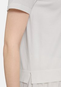 Biała bawełniana koszulka z krótkimi, podwiniętymi rękawami, o luźnym kroju, z bocznymi rozcięciami i gładką teksturą. Prosty design, bez wzorów.