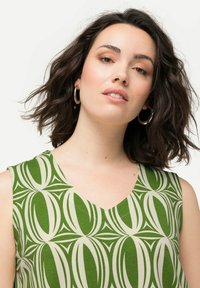 Mouwloze groene top met een V-hals en een geometrisch patroon in crème. Zachte stof met een gladde textuur en een ontspannen pasvorm.