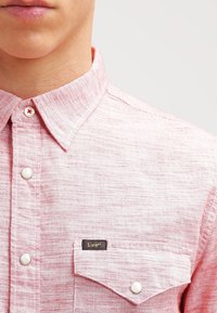 Camicia a maniche lunghe con fantasia rossa e bianca, colletto a punte, dotata di taschino e di un'etichetta nera con la scritta "Lee" sul lato sinistro.