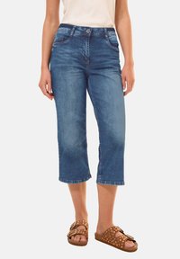 Jean cropped en denim bleu moyen, avec une fermeture par bouton et zip, cinq poches, et une coupe droite avec des ourlets nets.