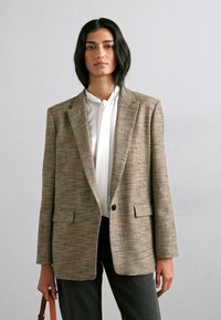 Rutet brun blazer med en struktureret silhuet, der har en enkelt knaplukning, notch revers og to frontlommer.
