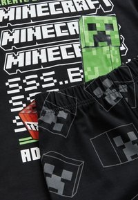 Minecraft-Themen schwarzes T-Shirt mit grünem Creeper-Grafik, weißem Text und schwarzen Shorts mit pixeligen Creeper-Gesichtern in Grau.