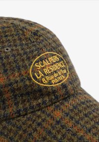 Gorro de lana con un patrón de pied de poule en verde, naranja y azul. Presenta un logo bordado en amarillo en la parte frontal. Superficie texturizada.
