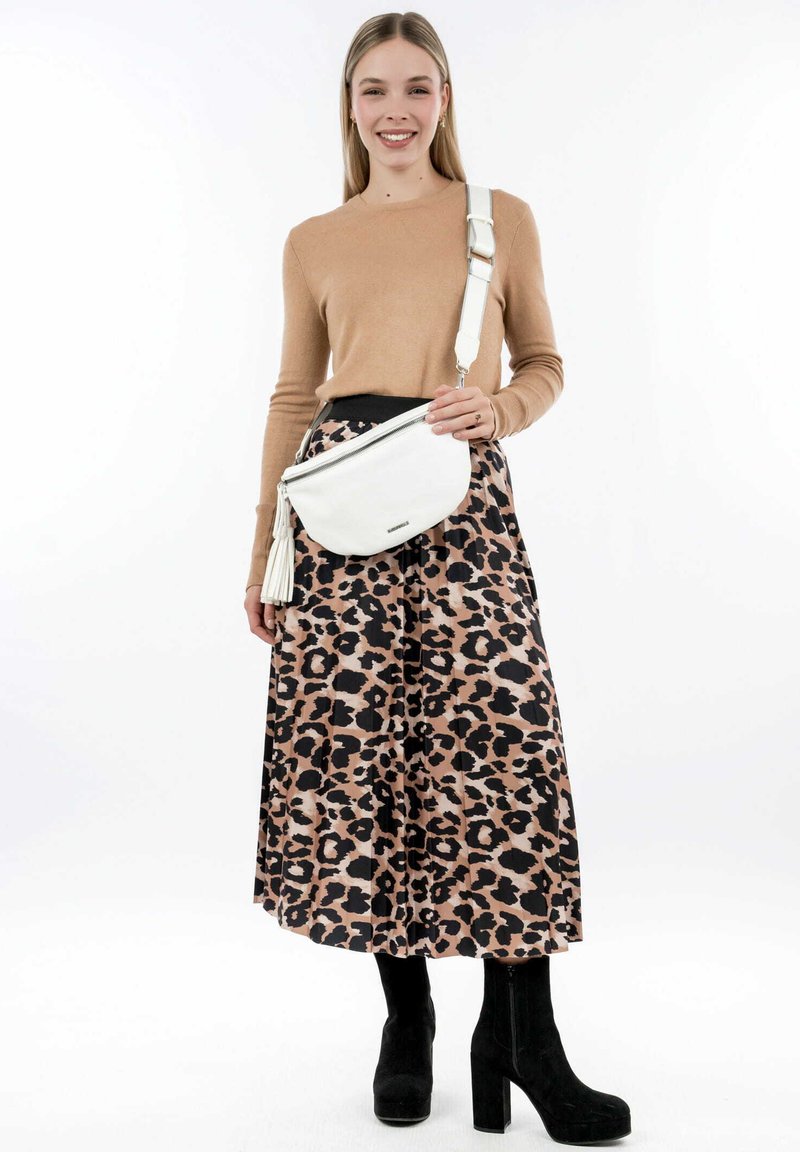 Bílá crossbody taška s zakřiveným designem a detailem v podobě třásní. Modelka má na sobě béžový svetr a sukni s leopardím potiskem, doplněnou černými botami na podpatku.