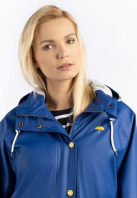 Blå vattentät jacka med dragsko på huvan, gula knappar och en broderad gul paraplylogotyp på bröstet. Grå inredningsfoder.