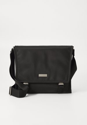 Sac messager noir en nylon avec une finition mate. Il dispose d'une fermeture à rabat, d'une sangle réglable et d'une petite plaque en métal avec logo.