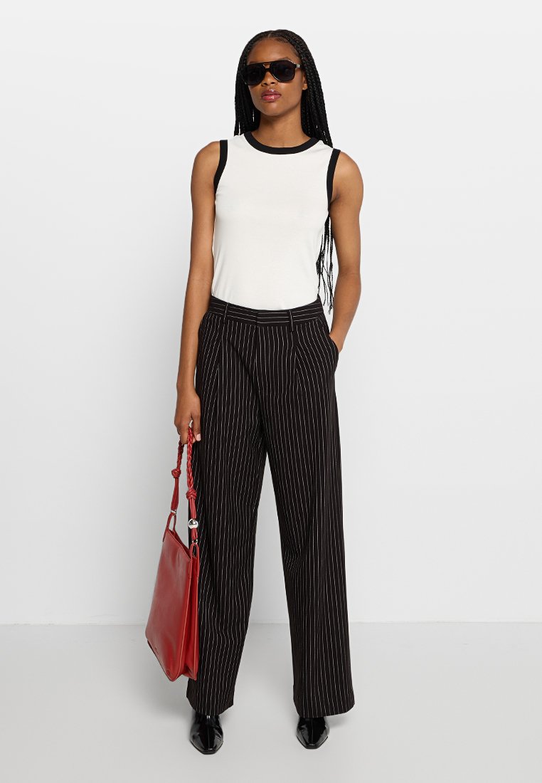 Biała bezrękawnikowa bluzka z czarnym wykończeniem, czarne szerokie spodnie w paski, oraz czerwona skórzana torebka. Modelka nosi okulary przeciwsłoneczne z prostymi włosami.