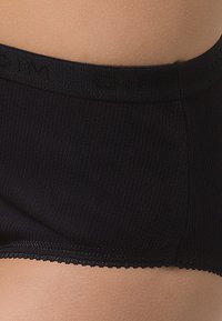 Black ribbed fabric brief with a smooth waistband and scalloped edges, featuring soft texture and form-fitting design.