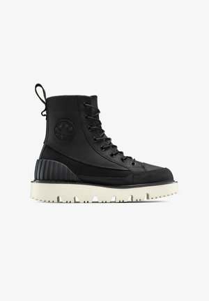Bota de combate negra con cordones, suela gruesa blanca con estrías, logo de estrella negra en el lateral, tira para tirar en la parte trasera y sección reforzada en el talón.