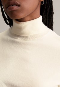 Cremfarbener, gerippter Rollkragenpullover aus weichem Stoff, mit taillierter Silhouette und hochgeschlossener Kragenform.