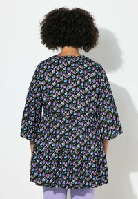 Sort blomsterkjole med klokkeærmer, der har lilla og blå mønstre. Blødt stof, løs pasform og detaljer med lagdelt kant.