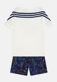 Completo per bambini composto da una maglietta bianca a maniche corte con strisce blu navy e pantaloni corti blu navy con stampe di personaggi colorati.