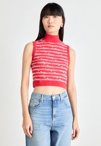 Crop top rouge à encolure haute avec un texte répétitif "tommy jeans" en blanc, associé à un jean taille haute bleu clair.