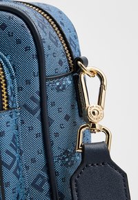 Niebieska torebka w wzory z teksturowaną powierzchnią, złotymi okuciami i odpinanym skórzanym paskiem z zapięciem na klips.