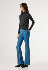 Top negro de manga larga con lunares blancos combinado con jeans ajustados azules acampanados. Botines negros de tacón realzan el conjunto.