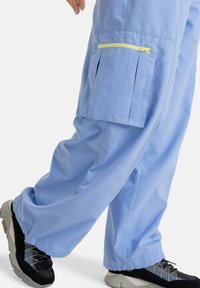 Lichtblauwe broek met een losse pasvorm, gemaakt van gladde stof. Bevat een gele ritszak en plooien aan de zijkant.