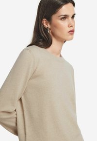 Beżowy sweter z dzianiny z długimi rękawami i okrągłym dekoltem, charakteryzujący się miękką teksturą i luźnym krojem. Prosty i uniwersalny design.