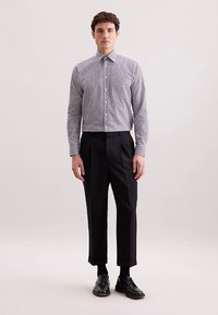 Koszula w kratę w czerni i bieli, zapinana na guziki, z długimi rękawami. Noszona z czarnymi plisowanymi spodniami i czarnymi sznurowanymi butami.