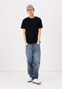 T-shirt nero a maniche corte, jeans in denim blu, cappellino da baseball grigio e sneakers bianche. Vestibilità casual con una silhouette rilassata.