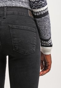 Jeans de mezclilla negros con un diseño ajustado, que cuentan con dos bolsillos traseros y un sutil detalle de costura. Llevados con un suéter de punto estampado.
