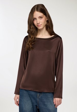 Maglietta marrone a maniche lunghe realizzata in tessuto morbido e lucido con una ampia scollatura a barca. Abbinata a jeans di denim blu larghi.