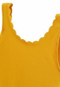 Haut jaune sans manches avec bords festonnés, fabriqué en tissu texturé, présentant un design uni et une apparence côtelée.