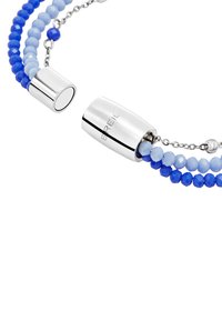 Armband med två trådar som har blå och ljusblå fasetterade pärlor, med silverfärgade metallaccenter. Inkluderar ett glatt, cylindriskt lås.