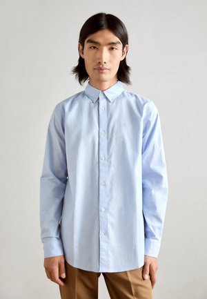 Light blue button-up shirt made of cotton. Features a collar, long sleeves, and white buttons. Small logo embroidered on the chest.