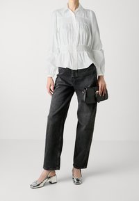 Weißes, langärmliges Hemd mit Knopfleiste und geraffter Taille, kombiniert mit lockeren schwarzen Jeans. Silbergraue Blockabsatzschuhe und eine kleine schwarze Handtasche.