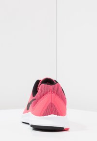 Baskets de course en mesh rose avec des accents noirs, présentant un talon arrondi, une surface texturée et une semelle intermédiaire blanche. Logo swoosh notable sur le côté.