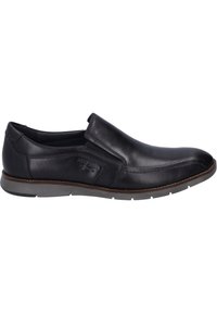 Zapato negro de piel sin cordones con perfil bajo, acentos elásticos en los lados, puntera curva y suela de goma gris claro con sutiles detalles de costura.