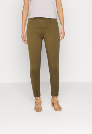 Jeans skinny verde-oliva com uma textura suave, design ajustado, estilo de cinco bolsos e cintura média, combinados com sapatos de tacão strappy bege.