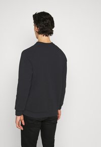 Sudadera gris oscuro con mangas largas, un escote redondo y costuras raglán, vista desde la espalda. Tejido suave con una textura lisa.