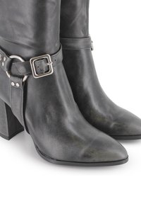 Botines de cuero negro hasta el tobillo con punta afilada, detalle de hebilla y correa plateada, acabado texturizado y tacón ancho.