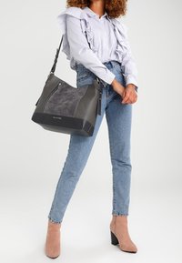 Duża szara torba na rękę z zamszowymi wstawkami, o gładkiej skórzanej fakturze, z bocznym zamkiem błyskawicznym i odpinanym paskiem na ramię.