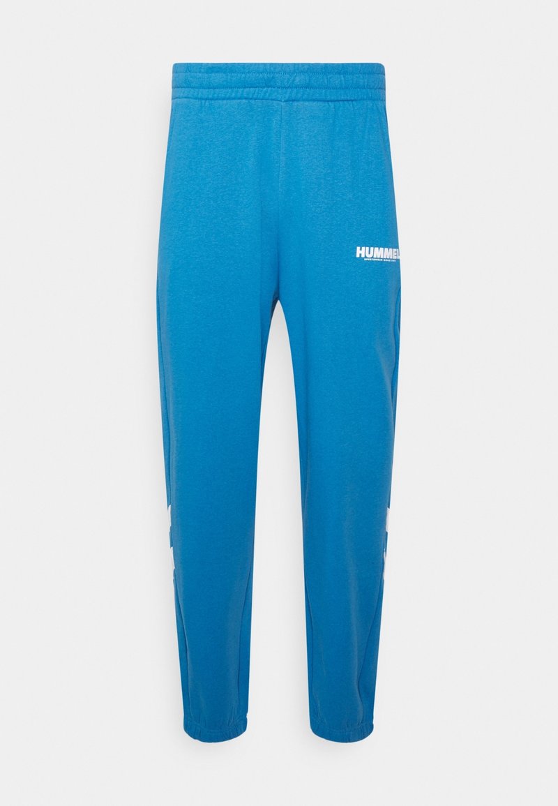 Blauwe sweatpants van zacht materiaal, met een elastische tailleband, taps toelopende pijpen en het witte "HUMMEL" logo op de dij.