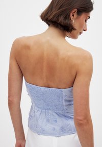 Helles blaues trägerloses Oberteil mit gestickten Blumenmustern und gerafftem Rückenteil. Der Stoff scheint weich mit einer leicht strukturierten Oberfläche zu sein.