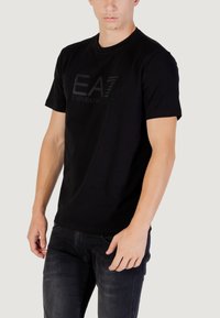 T-shirt nera a maniche corte, con logo EA7 testurizzato in tonalità scure. Realizzata in tessuto leggero, progettata per una vestibilità casual.
