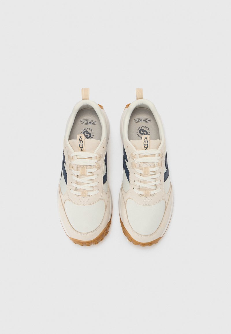 Beige Sneakers mit marineblauen Akzenten, runde Zehenform, Gummisohle und weißen Schnürsenkeln. Verfügt über Schlaufen für ein einfaches Anziehen und eine gepolsterte Innensohle.