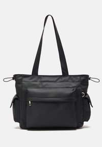 Black tote bag made of textured nylon. Features two handles, a front zip pocket, and side pockets. Minimalist design with no visible hardware.