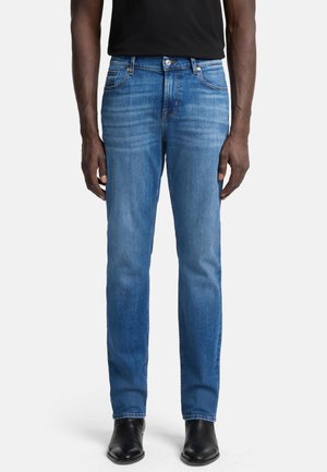 Enges Blau-Denim-Jeans mit geradem Bein, leichter Ausbleichung, fünf Taschen und Knopfverschluss. Kombiniert mit schwarzen Leder-Stiefeletten.