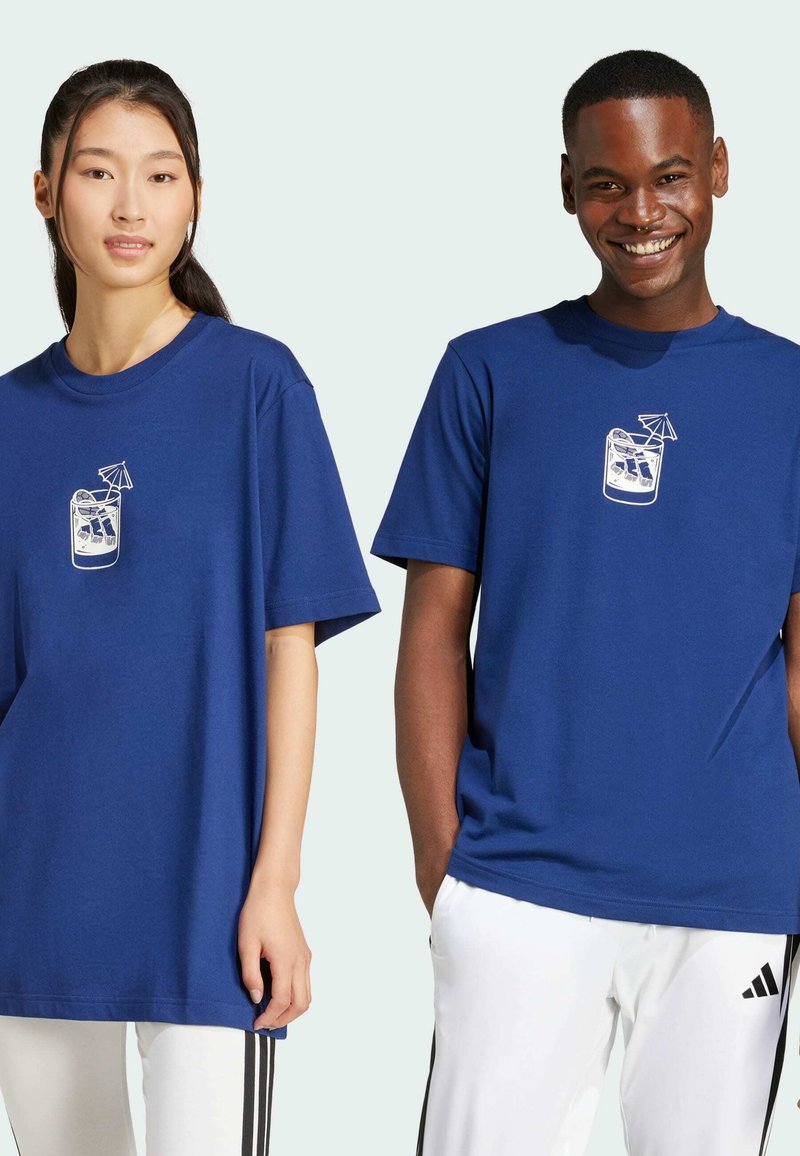 Due persone indossano t-shirt di cotone blu coordinate con una grafica bianca di una bevanda sulla parte anteriore. Le magliette hanno una vestibilità ampia e maniche corte.