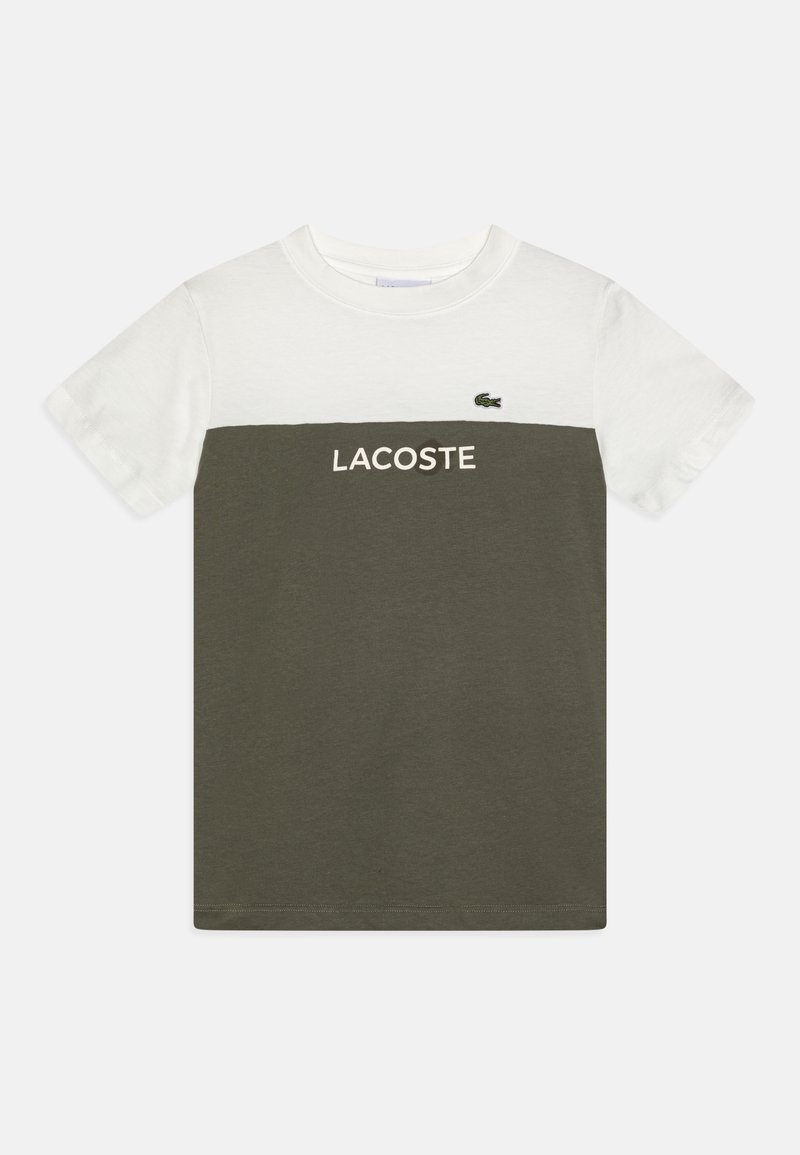 T-shirt à manches courtes avec une partie supérieure blanche et une partie inférieure vert olive, avec le texte « LACOSTE » et un petit logo crocodile sur la poitrine.