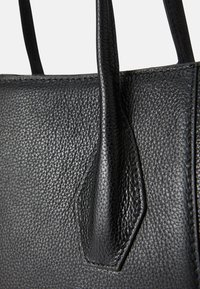 Black leather handbag featuring textured surface, smooth handles, and detailed stitching. Compact shape with a structured design.