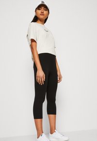 Világos bézs, cropped póló kis fekete grafikával, szűk fekete capri leggings-szel és fehér sportcipőkkel párosítva.